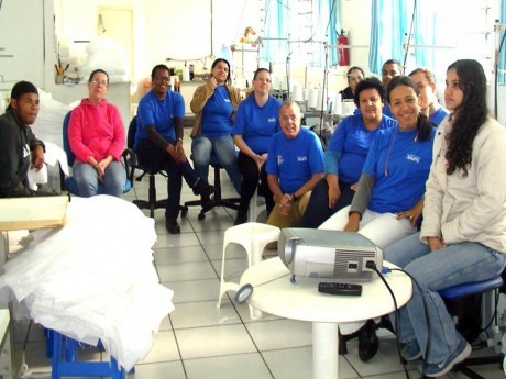 Reunião com funcionárias na própria área de confecção da “Industrial e Comercial MAP’S”, fabricante de almofadas e travesseiros. Vê-se que o capelão literalmente veste a camisa da empresa.