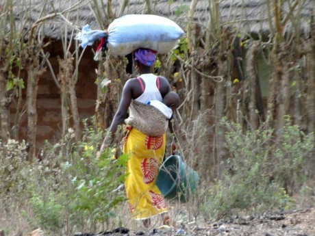Mulher típica guineense caminhando com filho e fardo na cabeça